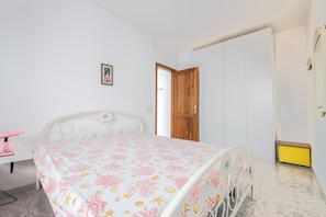 Une chambre à coucher avec un lit, un bureau doté d’une lampe rose, une porte en bois et une armoire jaune.