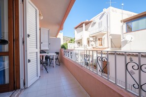 Un balcón con mesa y sillas, una puerta blanca y un edificio blanco con balcones.