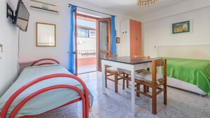 Une chambre avec un lit, une table, des chaises, un téléviseur, un climatiseur et une fenêtre avec des rideaux.