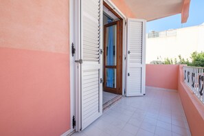 Un balcon avec des volets blancs, un sol carrelé et une vue sur le ciel.