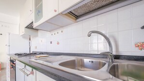 Une cuisine équipée d’un évier en acier inoxydable, d’une cuisinière à gaz et de meubles blancs.
