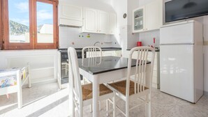 A kitchen with white cabinets, a dining table with chairs, a refrigerator, and a window with a view of buildings.