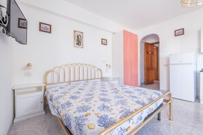 A bedroom with a bed, a wardrobe, a desk, and a refrigerator.