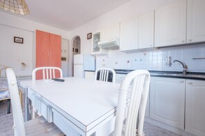 A modern kitchen with white cabinets, a white table, and a dining area with chairs.