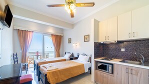 A hotel room with two beds, a dining table, a kitchenette, and a balcony with curtains. - Studio Apartment "Mazis Studio B2" with Sea View, Balcony & Wi-Fi (Corfu)