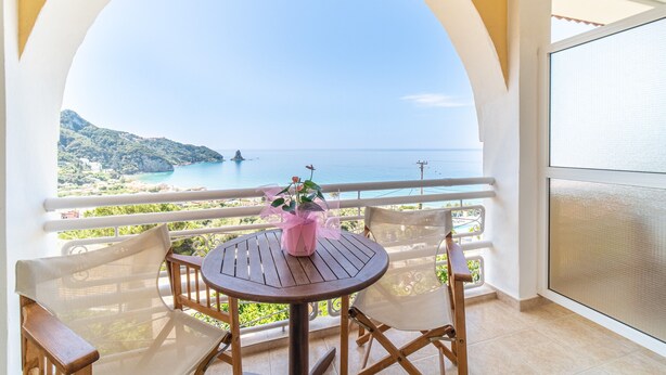 A balcony with a table and chairs, a potted plant, and a view of the sea and greenery. - Studio Apartment "Mazis Studio B2" with Sea View, Balcony & Wi-Fi (Corfu)