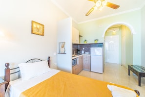 A bedroom with a bed, a bedside table, a ceiling fan, and a kitchen area with cabinets and appliances.