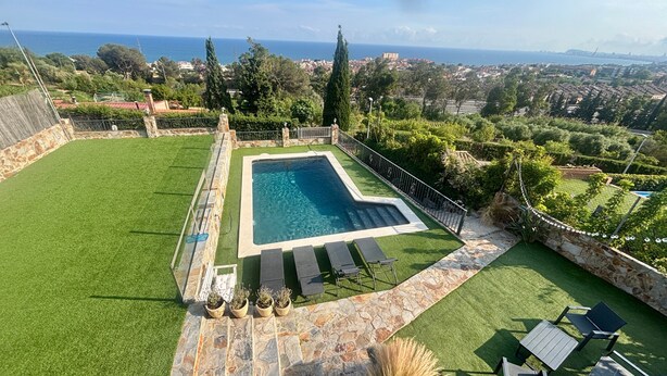A swimming pool with a stone border, surrounded by artificial grass and stone steps, with a view of the sea and distant buildings. - Holiday Home 'Villa Mar' with Sea View, Private Pool and Wi-Fi (Teià)