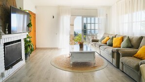 A living room with a fireplace, sofa, and a view through a large window. - Holiday Home 'Villa Mar' with Sea View, Private Pool and Wi-Fi (Teià)