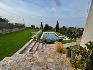A swimming pool with stone steps leading up to it, surrounded by a well-maintained lawn and potted plants.