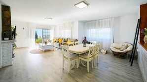 A spacious living area with a dining table, chairs, a sofa, and a large window. - Holiday Home 'Villa Mar' with Sea View, Private Pool and Wi-Fi (Teià)