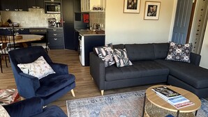 Ett modernt vardagsrum med en mörkblå soffa, ett runt soffbord och en mönstrad matta.