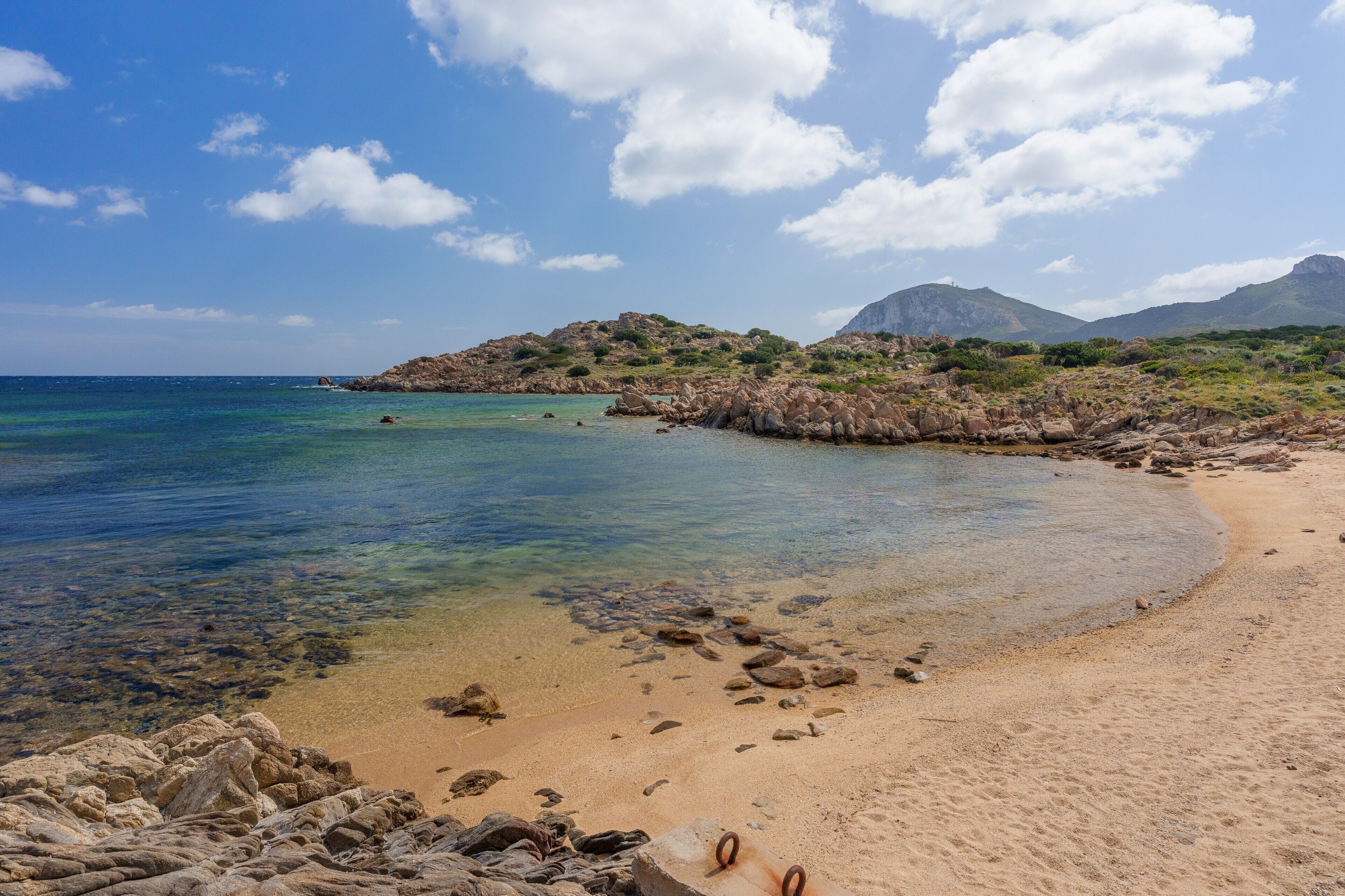 A beach with clear water, rocky shore, and mountains in the background.