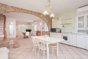 A spacious kitchen with white cabinets, a dining table with chairs, a stone archway, and a stone staircase.
