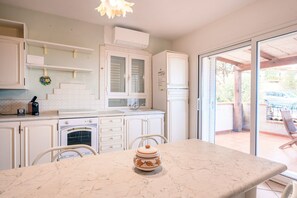 A kitchen with white cabinets, a marble countertop, a built-in oven, and a view through a glass door to an outdoor patio.