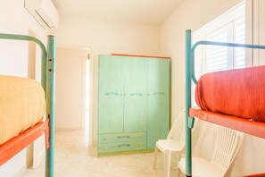 Une chambre avec des lits superposés, une armoire, une chaise et une porte donnant sur une autre pièce.