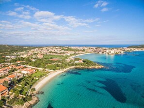 Vue aérienne d’une ville côtière avec une plage, des eaux d’un bleu limpide et des bâtiments aux toits rouges.