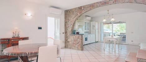 A spacious kitchen with a stone archway, white cabinetry, and a dining area with a round table and chairs.