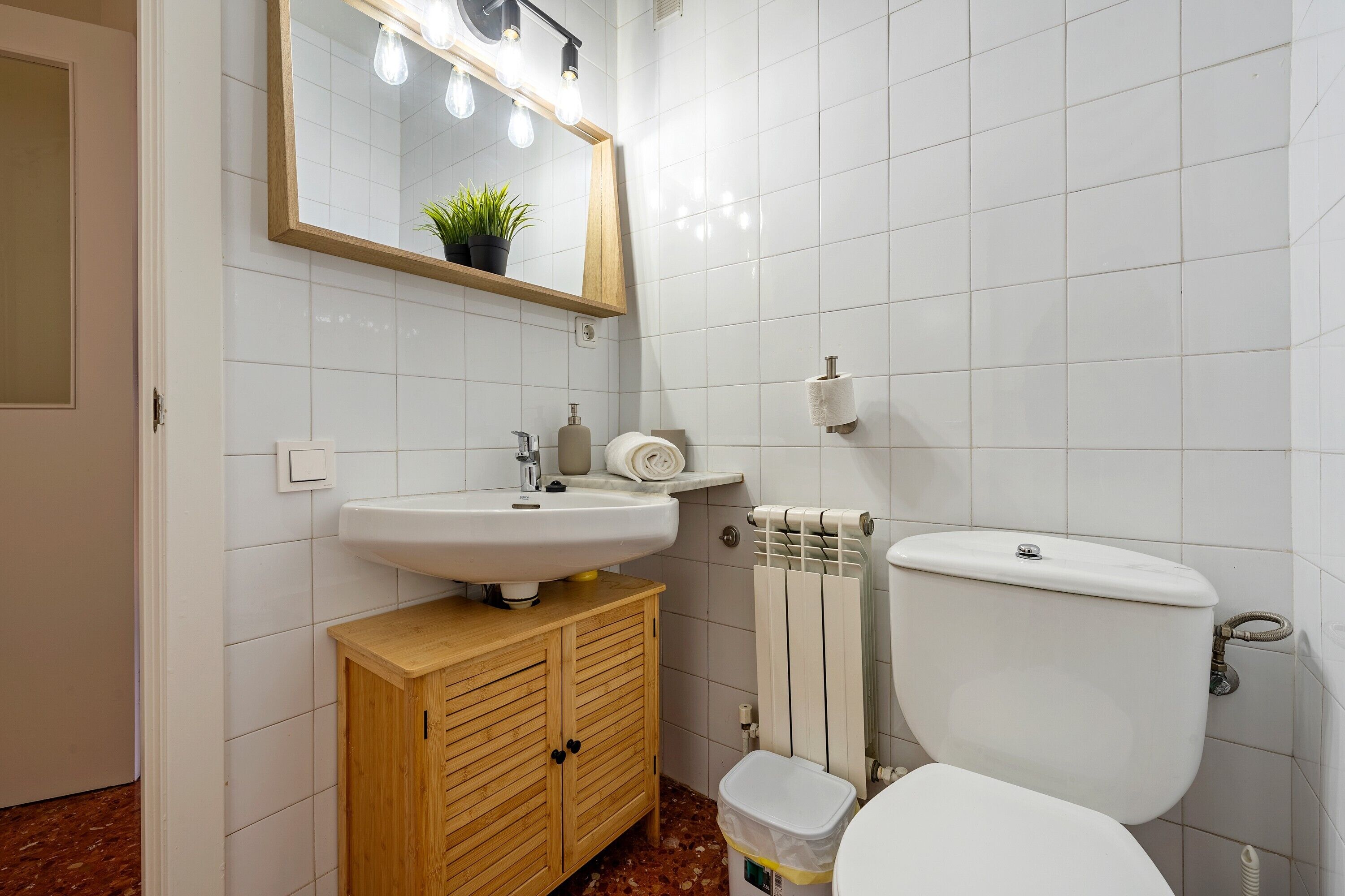 Un bagno con un lavandino bianco, un armadietto in legno, un water e uno specchio illuminato.