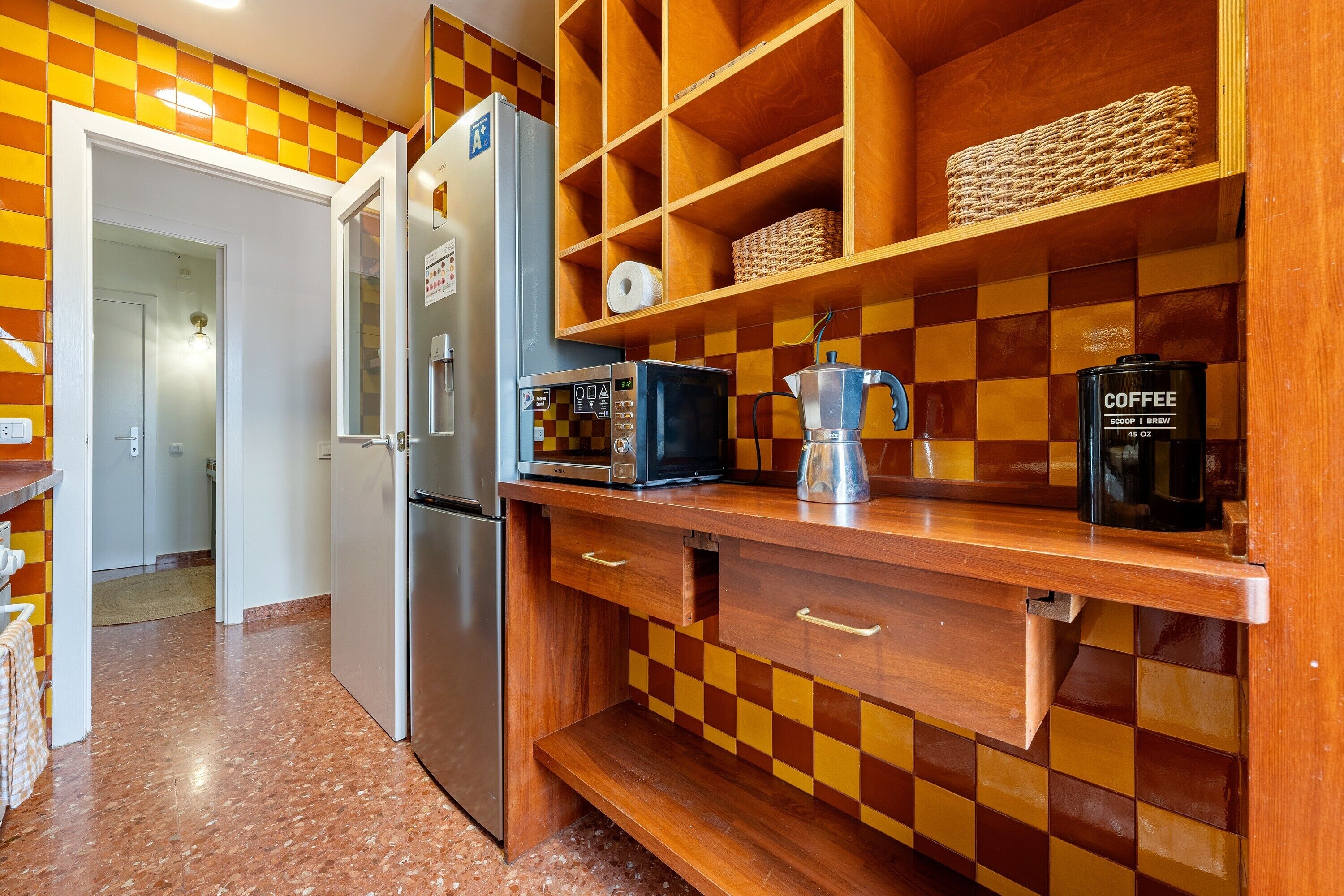 A kitchen with a refrigerator, microwave, coffee maker, and checkered wall tiles.