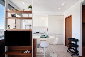 A modern kitchen with a TV, white bar stools, and a black cart. - Studio Apartment "Casa Alameda" with Sea View & Wi-Fi (Faro)
