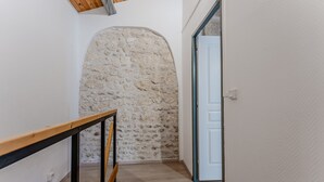 Un pasillo con una escalera de madera, un muro de piedra y una puerta blanca.