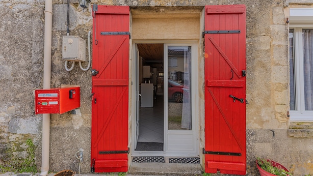 Un edificio con fachada de piedra, una puerta roja con bisagras negras y una pequeña ventana a la derecha.