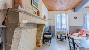 Una habitación con chimenea de piedra, vigas de madera en el techo, un sofá, una mesa de comedor y una silla.