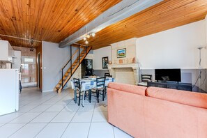 A spacious living area with a wooden ceiling, a dining table with chairs, a sofa, and a fireplace.