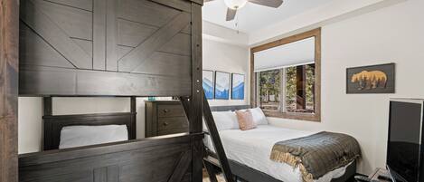 A bedroom with a bed, a ceiling fan, a TV, and a large mirror.