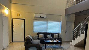 A living room with a sofa, coffee table, and a rug. There is a door and a window with blinds. - 🌴 Your Dream Getaway in the heart of Accra! Stay in this 3 Bedroom Property! 🏡 (Accra)