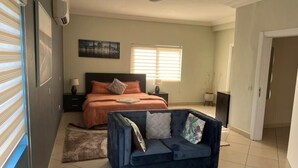 A bedroom with a bed, a dark blue sofa, a nightstand, a lamp, and a window with blinds. - 🌴 Your Dream Getaway in the heart of Accra! Stay in this 3 Bedroom Property! 🏡 (Accra)