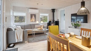 Un salon moderne comprenant un canapé, une table à manger avec des chaises, une cheminée et un téléviseur fixé au mur.