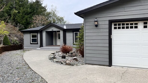 Ein zweigeschossiges Haus mit Garage, Auffahrt und einem angelegten Gartenbereich mit Steinen und Pflanzen.