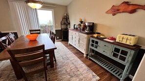 A kitchen with a wooden table, chairs, a rug, a cabinet with a toaster, and a decorative wall piece. - Secluded getaway 5 minutes from salmon fishing, kayaking, and whale watching! (Curry County)
