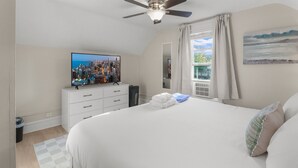 Une chambre avec un téléviseur diffusant des images de la ville, un lit avec des oreillers, un ventilateur de plafond et une fenêtre avec des rideaux.