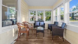 Une véranda avec de grandes fenêtres, des meubles en osier et un plancher en bois.