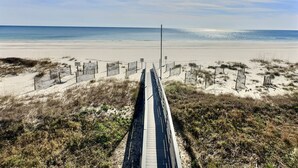 A beach with a wooden boardwalk leading to the shore, surrounded by sand and sparse vegetation. - Top of The World * Penthouse Views * Free Daily Activities! (Gulf Shores)
