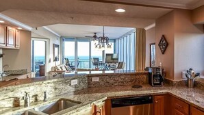 A kitchen with granite countertops, stainless steel appliances, wooden cabinets, and a view to the outside. - Top of The World * Penthouse Views * Free Daily Activities! (Gulf Shores)