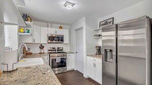 A modern kitchen with white cabinets, stainless steel appliances, a granite countertop, and a coffee-themed decor. - Luxury Loft Retreat: with Pool and Game room! (Houston)
