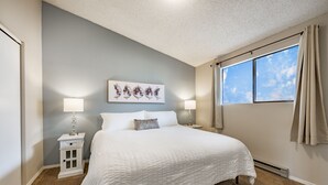 Une chambre à coucher avec un grand lit, deux tables de chevet, une commode, une fenêtre avec des rideaux et une œuvre d’art accrochée au mur.