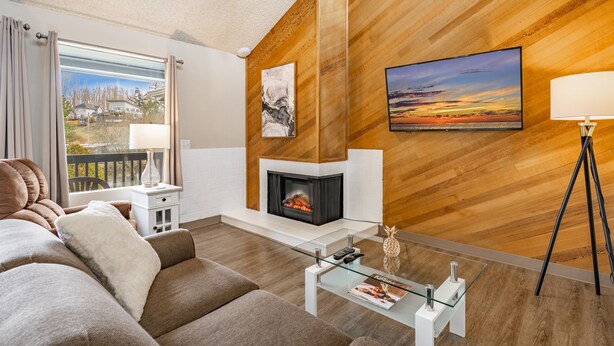Un salon moderne avec une cheminée, un canapé, une table basse en verre et une vue sur un balcon.