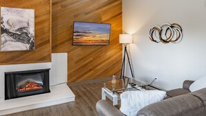 Un salon moderne avec une cheminée, un lambris en bois, un canapé, une table basse et un téléviseur.