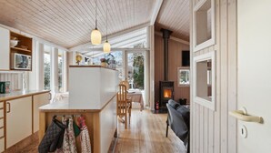 A cozy cabin interior with a wooden floor, a central island with chairs, a fireplace, and a kitchen area with a stove and cabinets. - 3 bedroom gorgeous home in Gilleleje (Gilleleje)