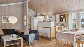 A modern, open-plan living and dining area with wooden flooring, a sofa, a coffee table, a dining table with chairs, and a kitchen area with cabinets and a microwave. - 3 bedroom gorgeous home in Gilleleje (Gilleleje)