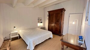 A bedroom with a bed, bedside lamps, a wooden wardrobe, a small table, and a mirror.