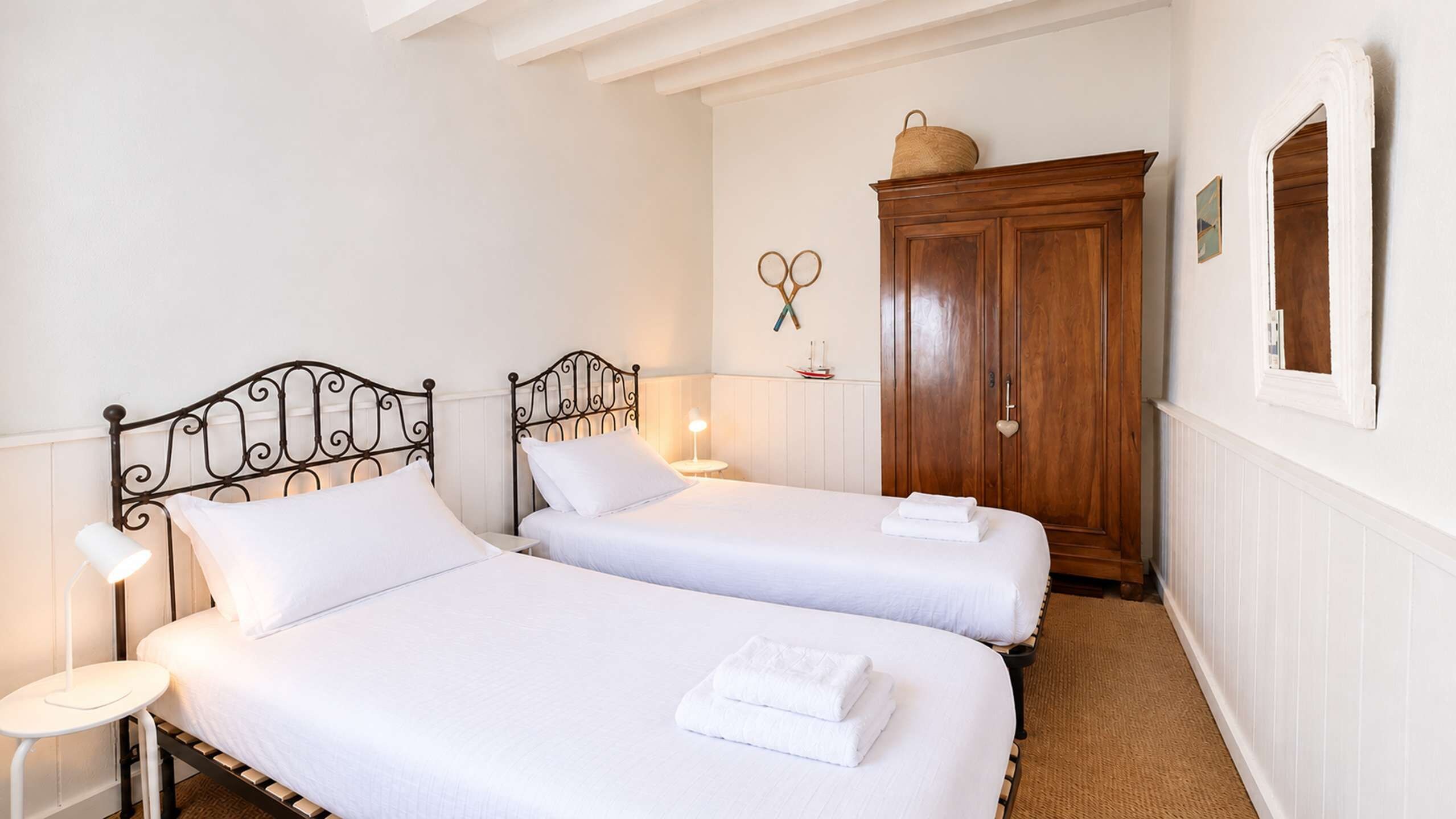 Een slaapkamer met twee bedden, een houten garderobe en een wandplank met een mand en een schaar.