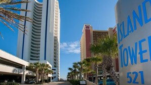 Un hotel llamado "Island Tower" con cielo despejado, palmeras y un área de estacionamiento.