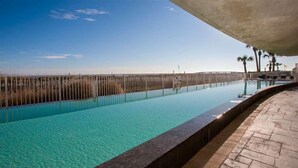 Una piscina con agua azul cristalina, una terraza de madera y vistas a la playa y palmeras.