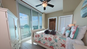 Un dormitorio con cama, ventilador de techo, ventana grande y vistas al exterior.